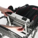 Person adjusting a metal frame on a wheelchair, tightening a small bolt near the seat rail.