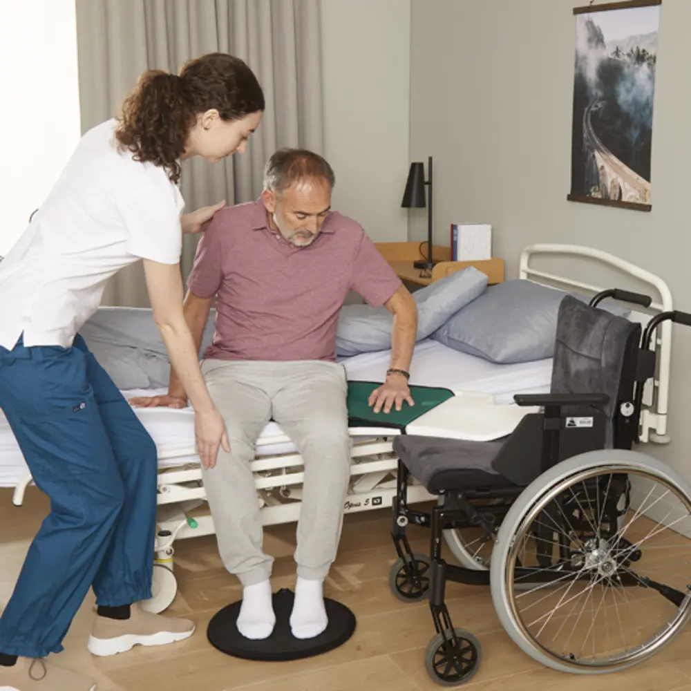 Immedia Butterfly45 - O Neill Healthcare Caregiver helps an elderly man stand on a round balance disc beside a hospital bed and wheelchair nearby.