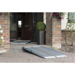 Metal portable wheelchair ramp at a brick-front porch, with another ramp folded nearby at the doorway.