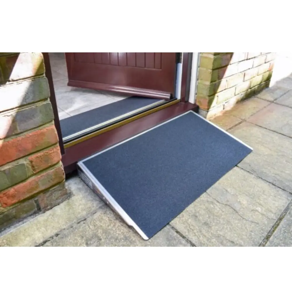 Doorline Threshold Wedge2 - O Neill Healthcare Portable blue wheelchair ramp positioned at a doorway threshold for accessible entry on a brick exterior wall and stone path.