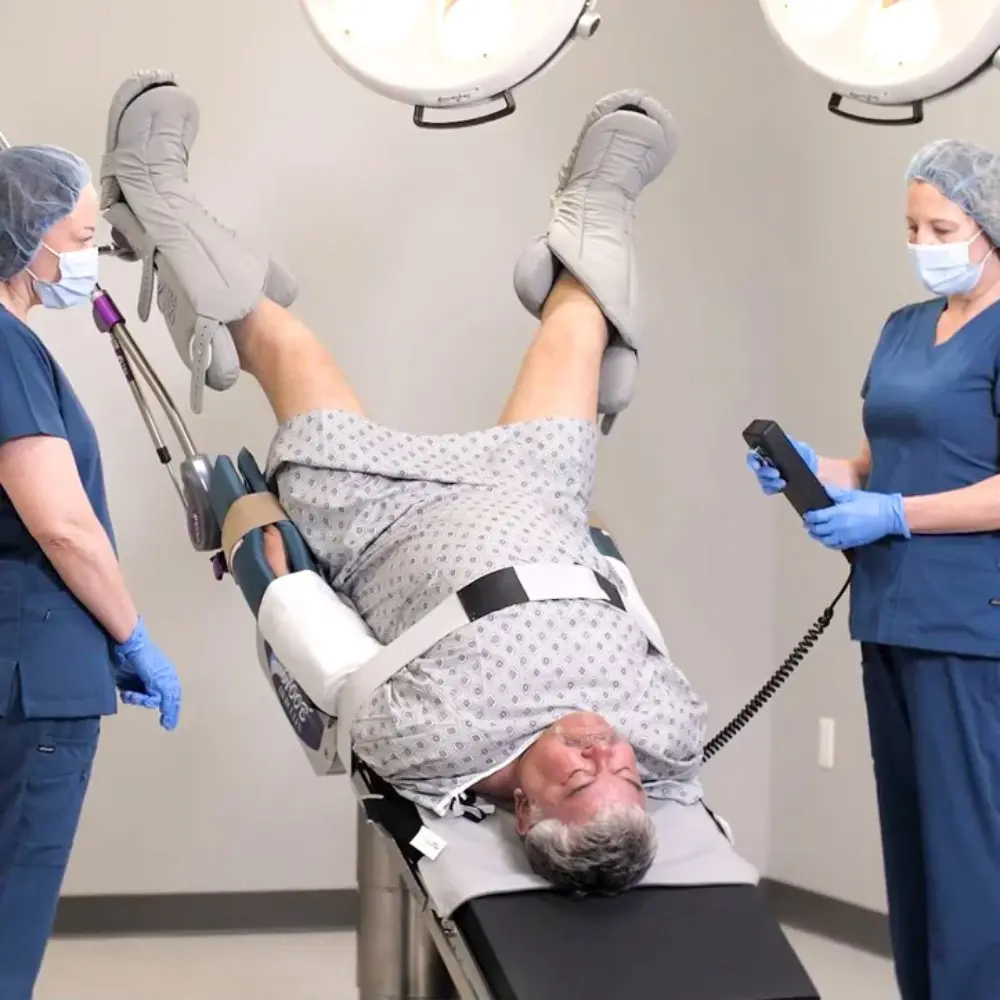 HoverMatt® T-Burg™ 3 - O Neill Healthcare Medical team assisting a patient in stirrups on an exam table during a procedure, monitored by staff with PPE and medical equipment nearby.