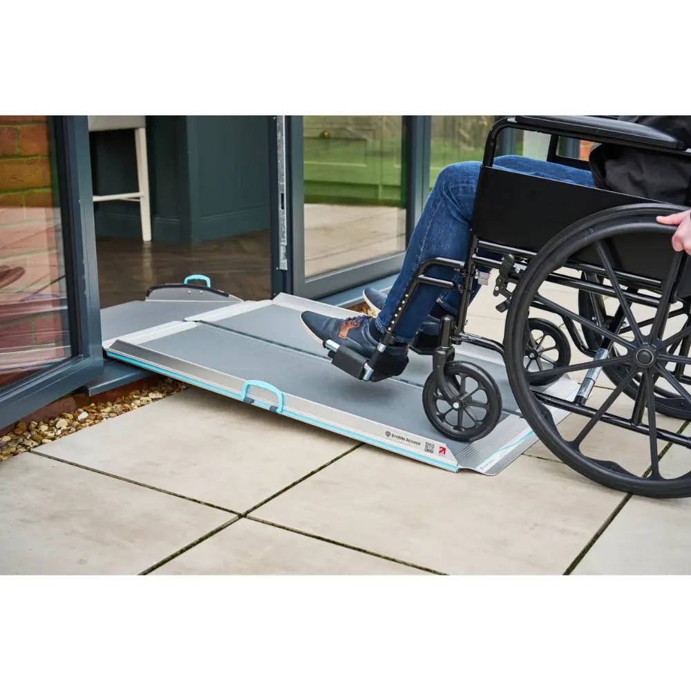 Aerolight Up Over 4 - O Neill Healthcare Wheelchair user rolling onto a metal portable ramp at a building entrance.