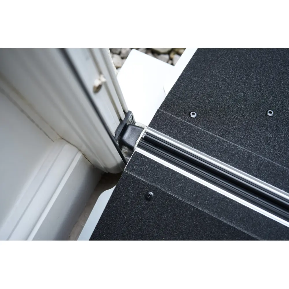 Doorline Butterfly Ramp 5 - O Neill Healthcare Close-up of a door threshold showing a black textured panel, metal guide rail, and weatherstrip at the frame edge in view of a doorway